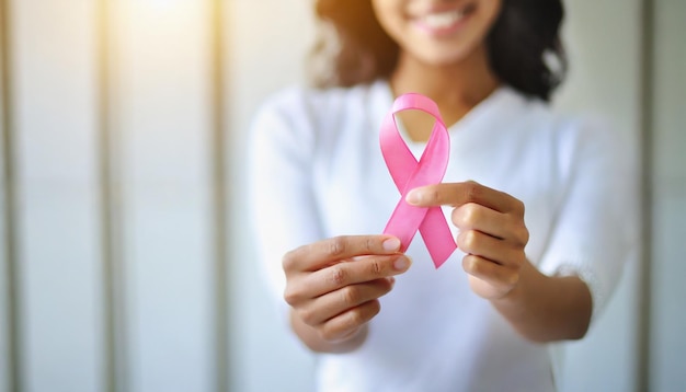 A mão da mulher segura uma fita rosa que simboliza a conscientização e os cuidados médicos para o câncer de mama