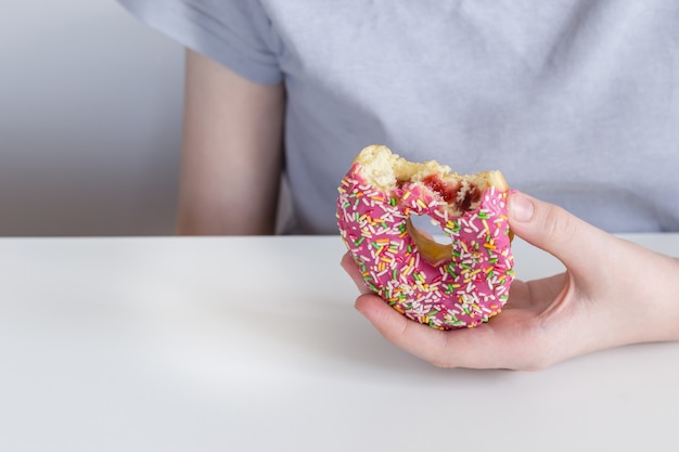 A mão das crianças estica o donut mordido com cobertura rosa e recheio de geléia.