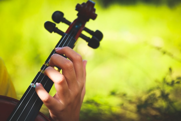 A mão das crianças que guarda a corda do violino que joga no jardim.