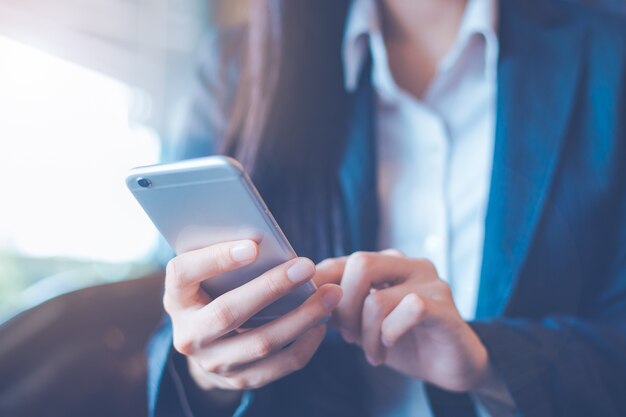 A mão das mulheres de negócio está usando telefones celulares no escritório.