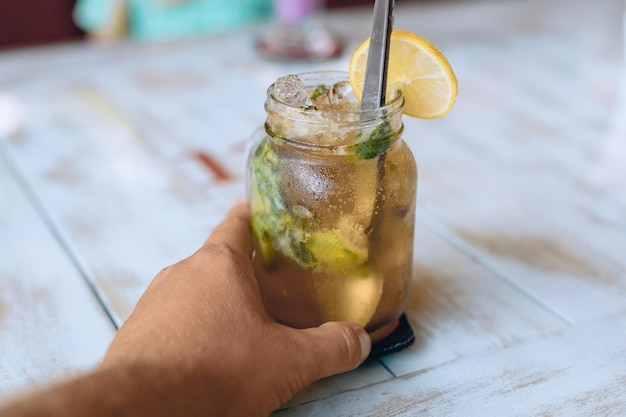 A mão de macho está segurando um copo de suco fresco com uma rodela de limão na borda