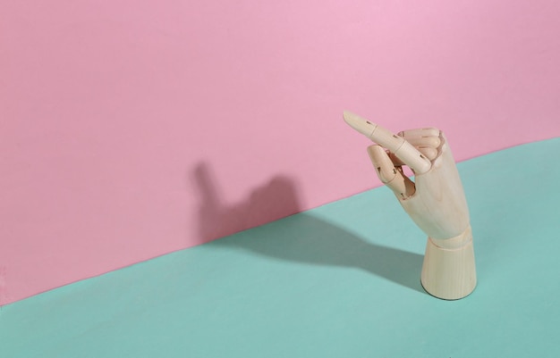 A mão de madeira aponta o dedo no fundo pastel rosa azul Sombra na moda Arte conceitual Minimalismo
