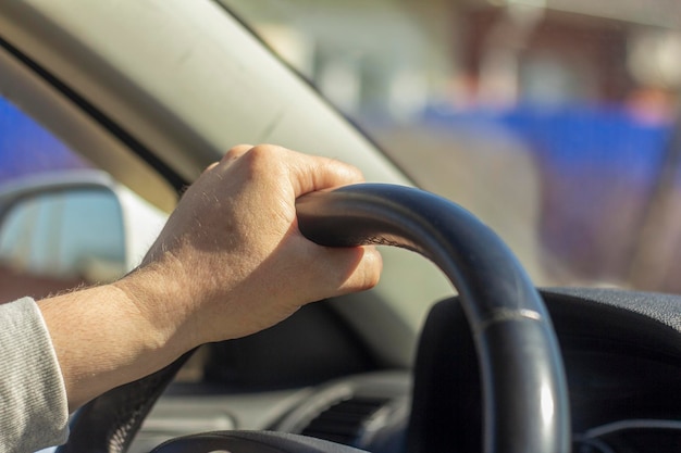 A mão de um homem adulto no volante à luz do sol.