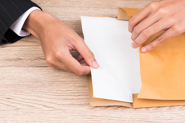 A mão de um homem de negócios abre um envelope marrom em uma mesa.