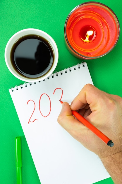 Foto a mão de um homem desenha o ano seguinte em um caderno com uma caneta hidrográfica vermelha. decoração de reveillon.