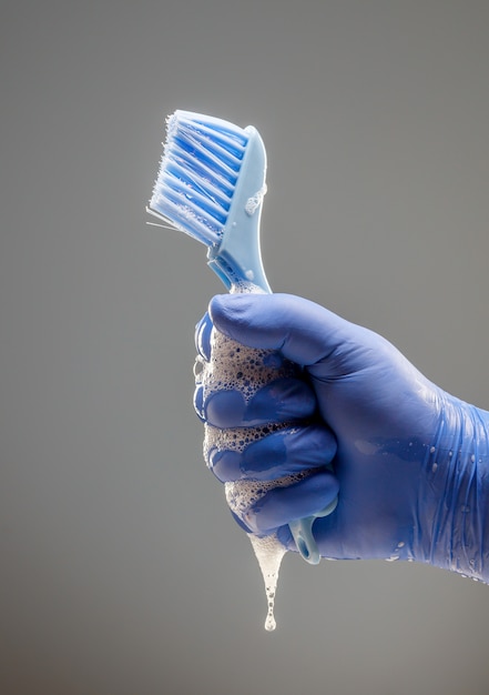 A mão de um homem em uma luva azul segura uma escova para limpeza