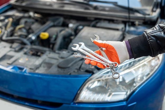 A mão de um homem em uma luva especial segura ferramentas para um carro perto do carro. Conceito de ferramentas. Conceito de conserto de carro