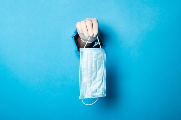 Foto a mão de um homem em uma luva médica segura uma máscara médica em azul