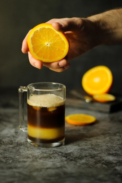 A mão de um homem espreme o suco de uma laranja fresca em um copo de café gelado bumble