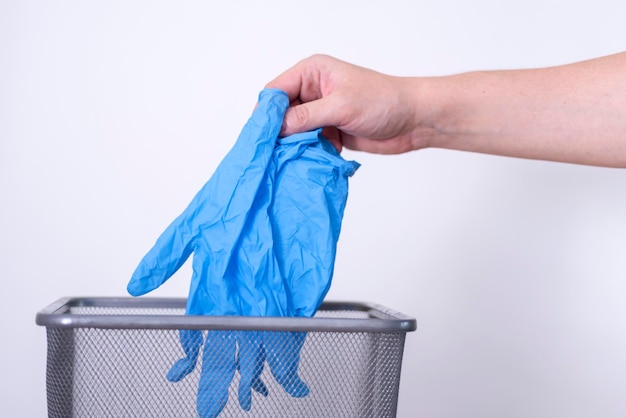 A mão de um homem joga luvas médicas azuis em uma lata de lixo contra um fundo cinza