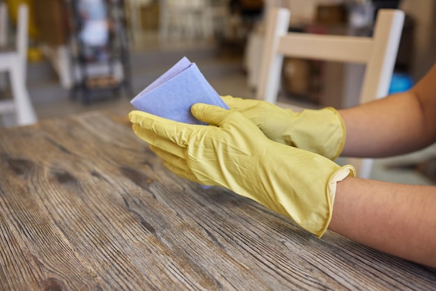 A mão de um homem na luva médica limpa a mesa com guardanapo Garçom de fundo em um avental em desfoque Tratamento de superfície