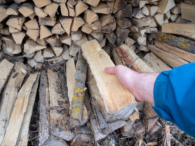 A mão de um homem segura um tronco puxado de uma pilha de lenha