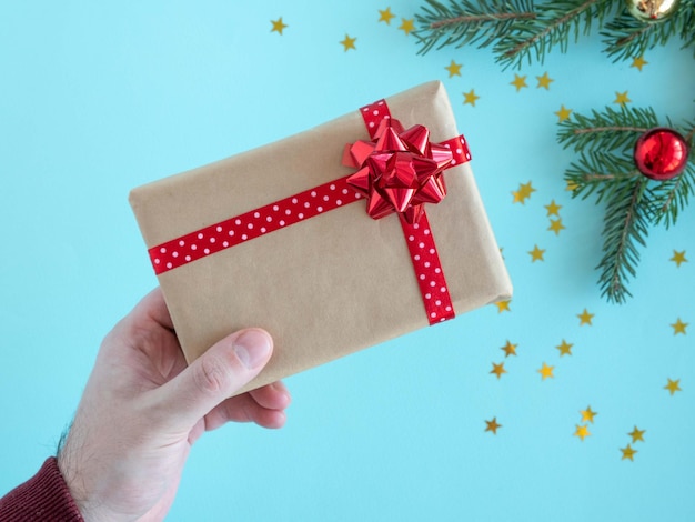 A mão de um homem segura uma caixa de presente com um laço vermelho em um fundo de Natal.