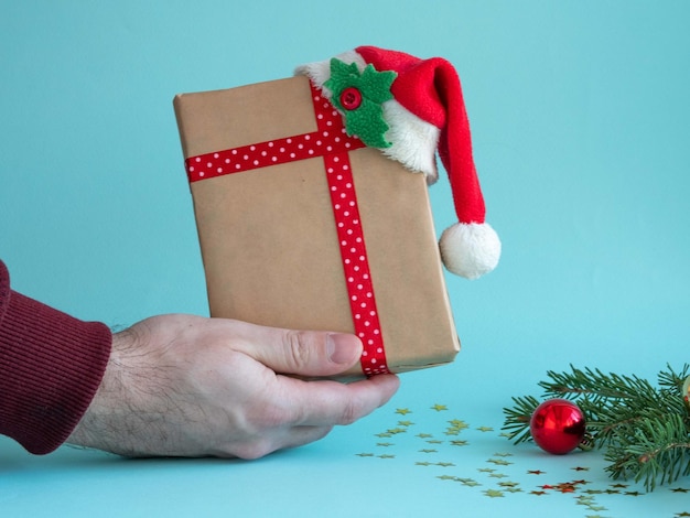 A mão de um homem segura uma caixa de presente com um laço vermelho em um fundo de Natal.