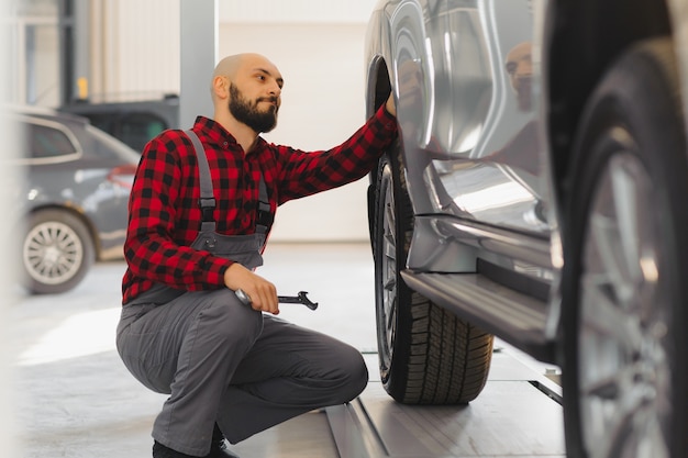 A mão de um mecânico de automóveis com uma chave inglesa em uma zona combinada perto do carro na oficina