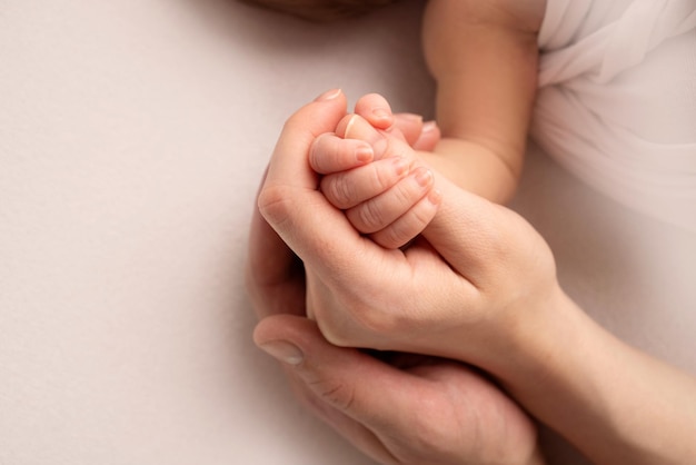 A mão de um recém-nascido dormindo na mão da mãe e do pai close-up. Dedos minúsculos de um recém-nascido. A família está de mãos dadas. Fotografia macro de estúdio. Conceitos de família e amor.