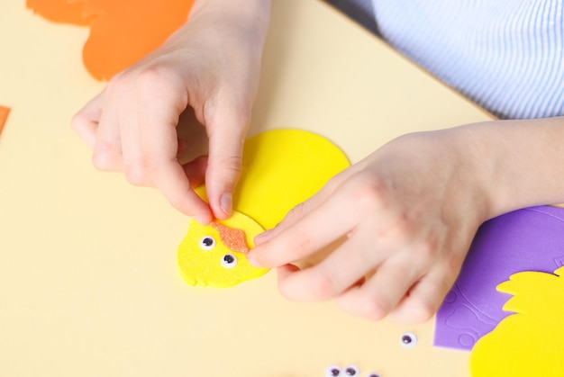 A mão de uma adolescente caucasiana cola um adesivo de bico de pássaro de feltro laranja com os dedos