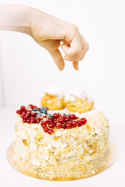 a mão de uma criança alcança um pedaço de bolo. bolo de napoleão caseiro decorado com frutas. delicioso