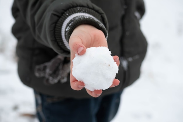 A mão de uma criança segurando uma bola de neve redonda.