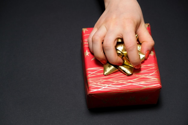 A mão de uma mulher agarra uma caixa de presente por um arco em um fundo preto