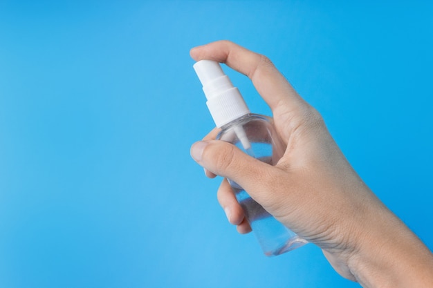 A mão de uma mulher com um anti-séptico em um close-up de fundo azul. O conceito de higiene e limpeza. Desinfetante