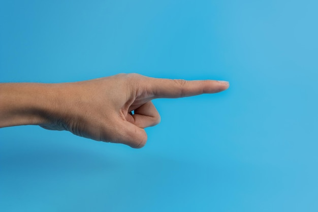 A mão de uma mulher com um dedo indicador em um fundo azul. Copie o espaço.