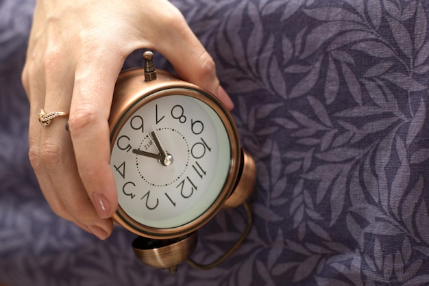 A mão de uma mulher com um despertador pendurado na cama o conceito de um despertar difícil cedo