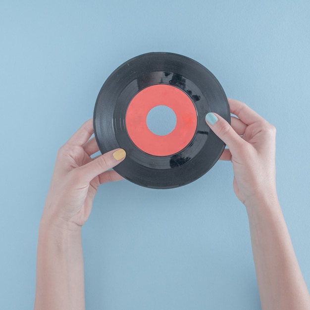 A mão de uma mulher com um disco de gramofone em fundo azul pastel. arte abstrata. ideia de decoração criativa mínima com espaço de cópia