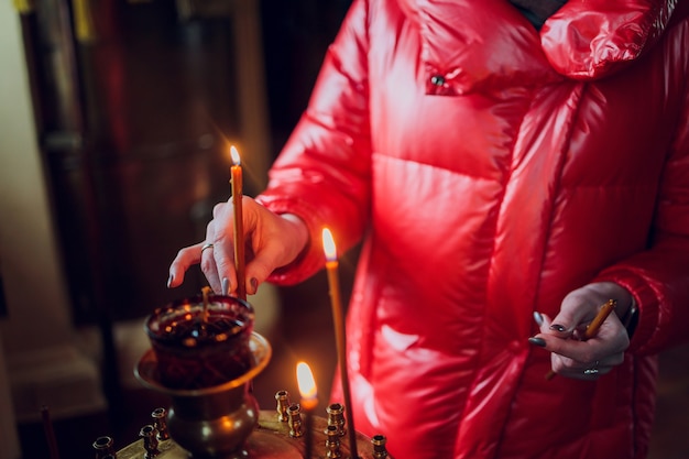 A mão de uma mulher com uma jaqueta vermelha coloca uma vela da igreja.