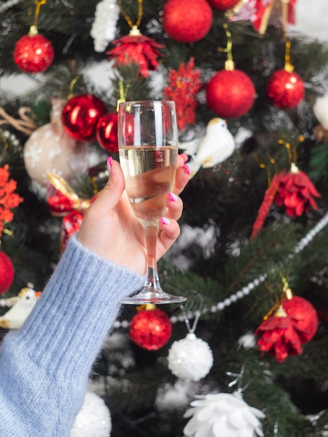 A mão de uma mulher com uma taça de champanhe e uma árvore de Natal decorada