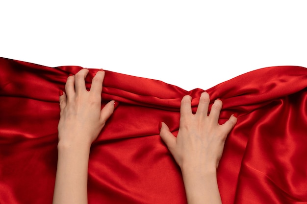 Foto a mão de uma mulher com unhas vermelhas está tentando arrancar o tecido de seda vermelha