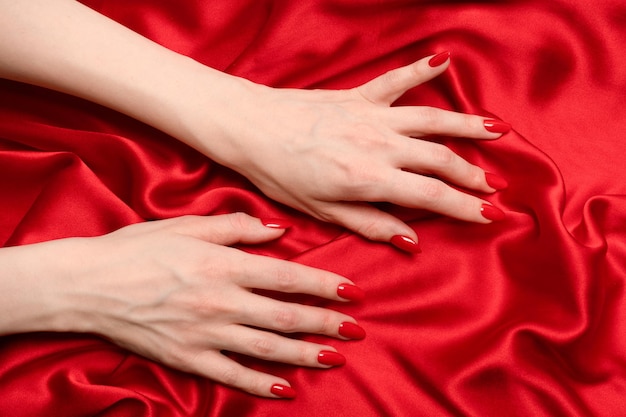 A mão de uma mulher com unhas vermelhas está tentando arrancar um tecido de seda vermelho