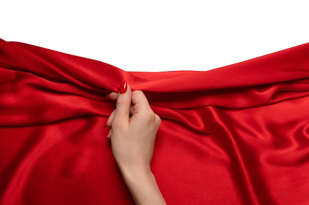 Foto a mão de uma mulher com unhas vermelhas está tentando arrancar um tecido de seda vermelho