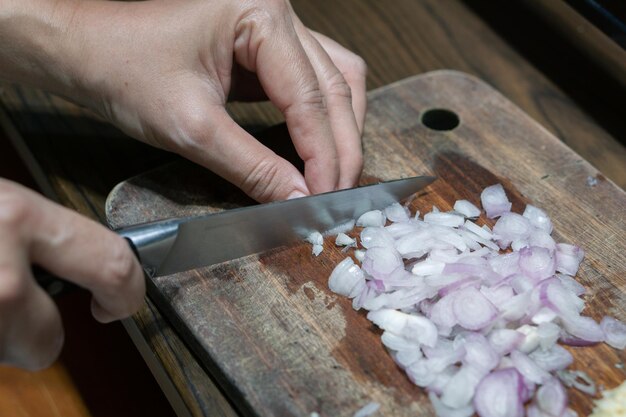 A mão de uma mulher cortou cebolas vermelhas na tábua de cortar na cozinha de casa Detalhe da mulher cortando cebola roxa