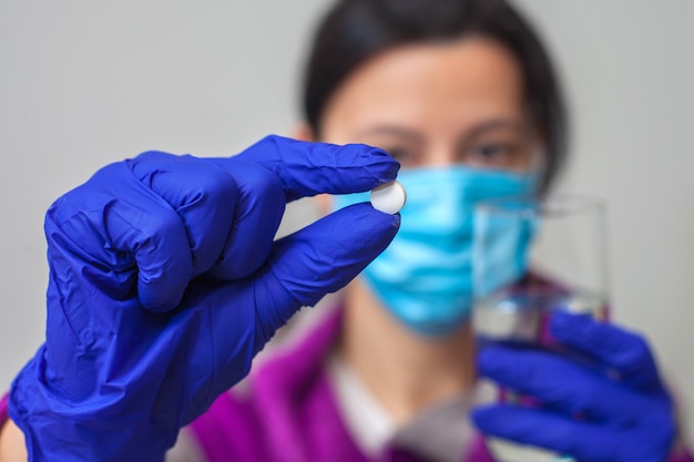 A mão de uma mulher em uma máscara protetora e uma luva azul médica segura uma pastilha branca com os dedos