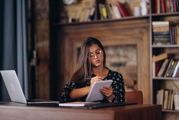 A mão de uma mulher escrevendo em um caderno branco em branco na mesa.