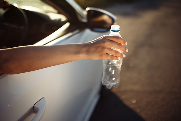 a mão de uma mulher jogando uma garrafa de plástico pela janela do carro.