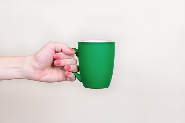 A mão de uma mulher segura uma caneca verde com uma superfície fosca em um fundo bege neutro. Modelo para inserir texto ou imagens na caneca. Bom dia conceito, potencializando a vitalidade com café ou chá.