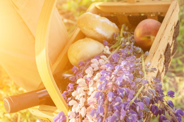 A mão de uma mulher segura uma cesta de piquenique com vista superior de vinho de comida de flores