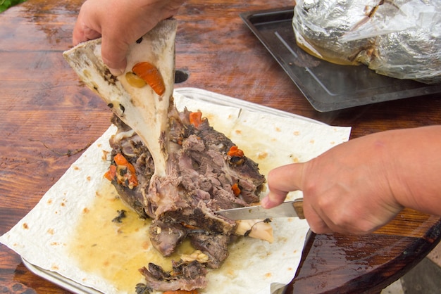 A mão de uma mulher separa a carne frita dos ossos, cortando-a com uma faca. Carne deliciosa para jantar em família