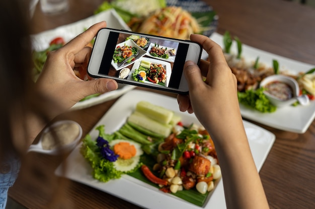 A mão de uma mulher tira fotos de alimentos feitos por ela mesma. Os vendedores de alimentos tiram fotos com um smartphone para postar no site de pedidos de comida online.