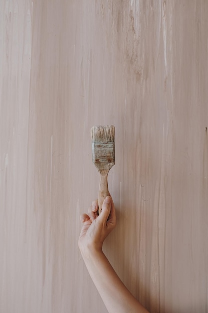 A mão de uma pessoa segura o pincel de pintura contra a parede bege rosa neutra Conceito de criação de arte estética Fundo de pintor de artista minimalista