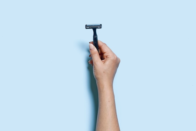 A mão de uma pessoa segura uma lâmina de barbear de uso múltiplo em uma vista de fundo azul vista de cima