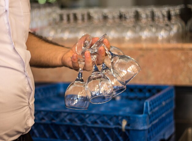 A mão do barman segura os muitos copos de vinho de perto