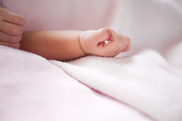 A mão do bebê recém-nascido no cobertor rosa em tom de cor suave