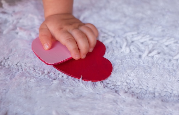 A mão do bebê segura corações em um fundo branco. Uma criança tenta agarrar corações de um tapete branco fofo