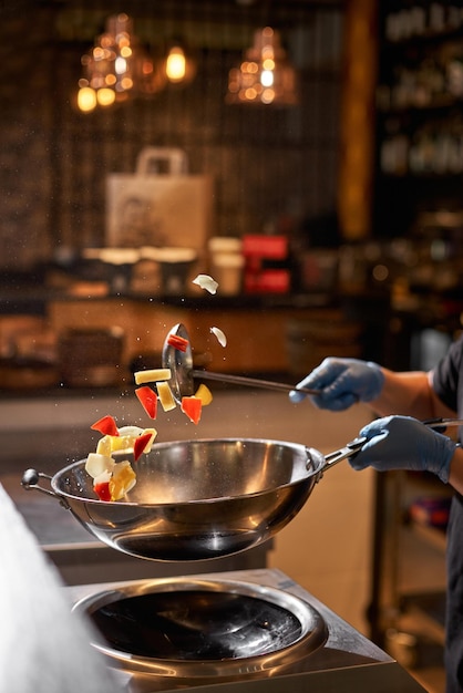 A mão do chef mantém as mãos fechadas jogando comida na cozinha escura profissional Chef preparando comida asiática