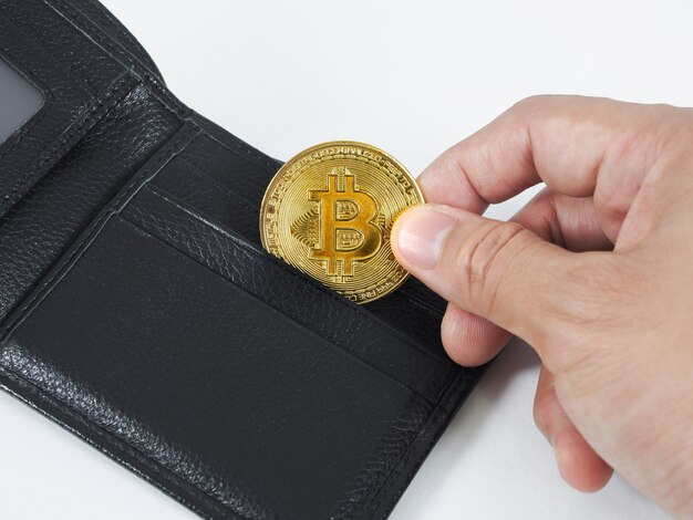 A mão do close up pega o bitcoin dourado no fundo branco da carteira