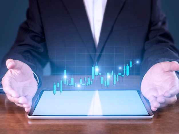 A mão do empresário apresenta o crescimento do gráfico do mercado de ações de análise do tablet e o aumento dos indicadores positivos do gráfico Mão segurando o tablet mostra o gráfico de ações no fundo azul