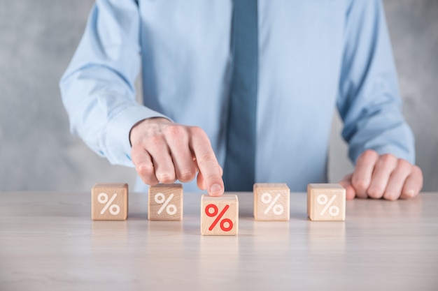 A mão do empresário pega um bloco de cubo de madeira representando, mostrado o ícone do símbolo de porcentagem. Conceito de taxas financeiras e hipotecas de taxa de juros.